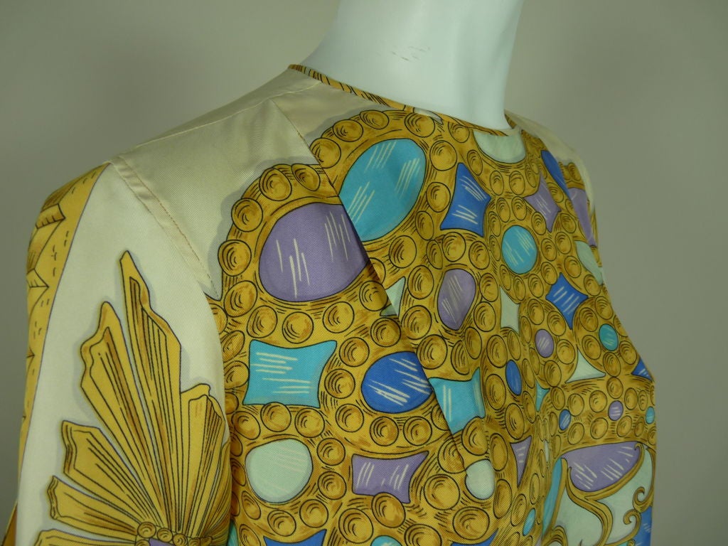 Lovely printed silk blouse from Emilio Pucci featuring a trompe l'oeil Faberge Egg-style bejeweled motif in shades of blue, violet and gold on an ivory ground. Hem is scalloped to mimic the pattern of the print. Short sleeves tie at hem and are slit