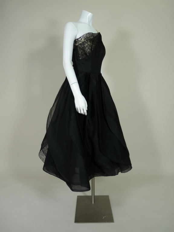 Spectacular 1950's black silk organza cocktail dress from Elizabeth Arden. Asymmetrical one shoulder bodice is silk organza with a peek-a-boo double layer panel of black french lace at bust and pale peach velvet strap detail. Bodice has boning at