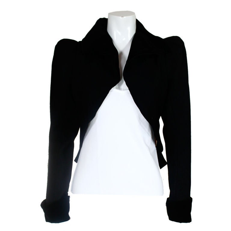 Cropped equestrian style black twill jacket from Vivienne Westwood is trimmed in black velveteen at the lapel and cuffs. Shoulders are padded and pleated for added structure. Front collar cascades to the back of the jacket into a pleated peplum.