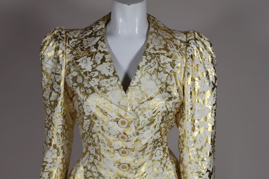Metallic gold silk screened silk floral evening jacket from Yves Saint Laurent has white and gold enamel figural flower buttons, slightly padded shoulders and exaggerated cuffs. <br />
<br />
Measurements--<br />
Bust: 36