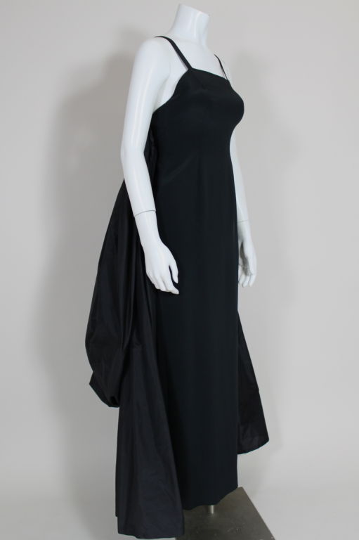 Statement making black silk gown from Bill Blass features a fitted column dress with attached cascading silk taffeta bustle. Bustle is comprised of two layers, the first is secured to the gown down the side seams, and the second is a continuous