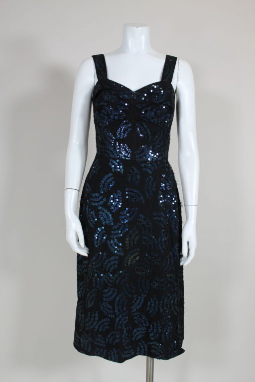 Gorgeous ensemble from legendary designer, Adrian, features a shimmering, sequined tulle cocktail dress with a matching jacket. Dress is crafted from black tulle layered over black crepe, which has been embroidered all over with midnight blue