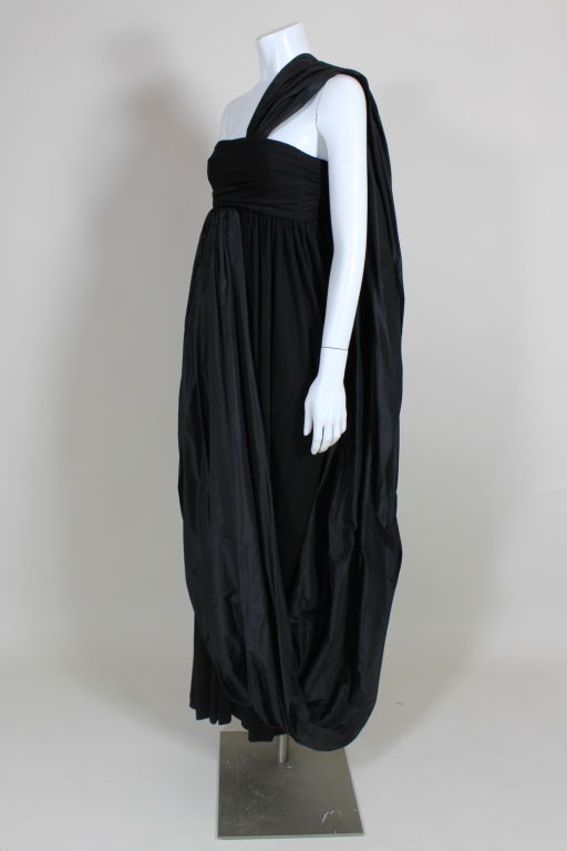 Dramatic black jersey evening gown from Bill Blass has a voluminous taffeta shoulder drape that extends from the top of the bodice all the way around to under the bust. Empire waist bodice is ruched from the side seams. Skirt is gathered from the