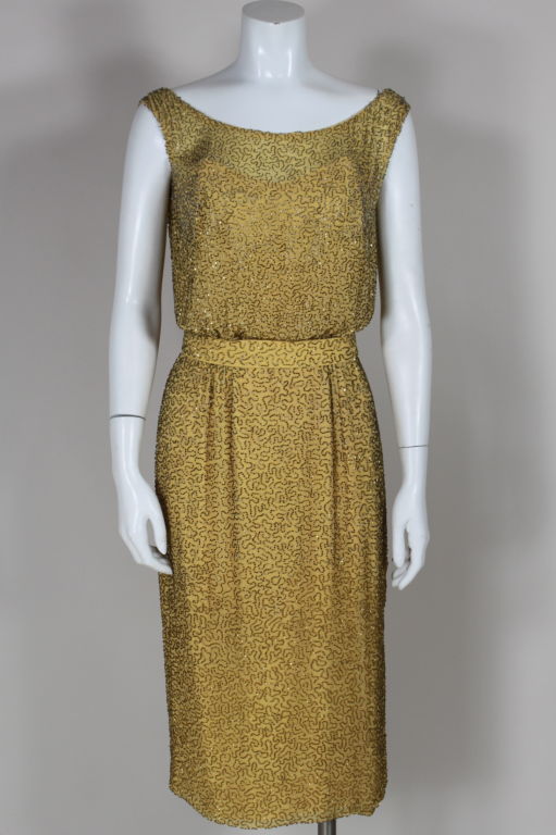 Circa 1950's golden yellow crinkle chiffon cocktail dress from Ceil Chapman is entirely embroidered with gold colored glass beads in a serpentine pattern. Sleeveless bodice has a slight blouson silhouette and skirt is a slim pencil style. Fully