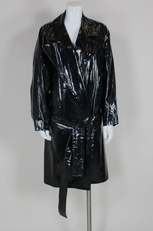 Chic, belted, black vinyl trench coat from Yves Saint Laurent has a dramatic, over-sized lapel and drop shoulders. Coat is belted at the hip to add to the slouchy, effortless silhouette. Seams are accented with a row of topstitching. Two front slash