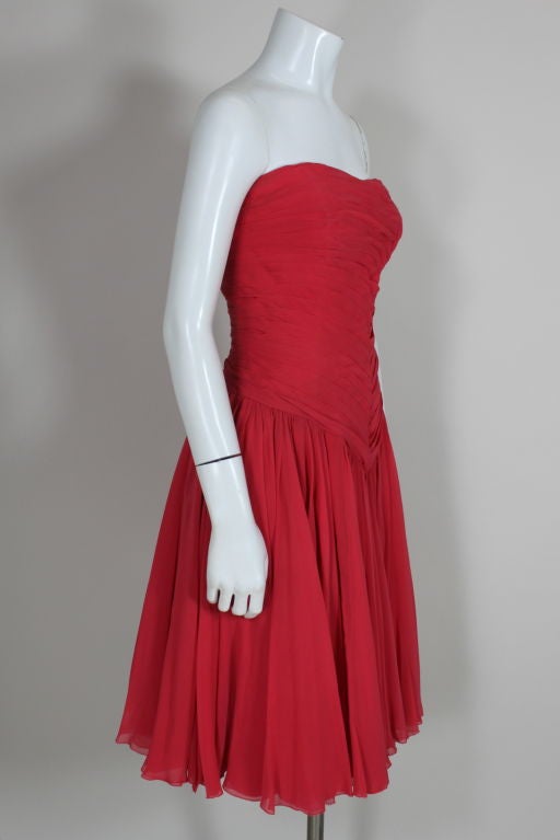 Brilliant coral red silk cocktail dress from French couturier Jean Desses features an asymmetrically hand pleated bodice. Flouncy layers of silk give the softly pleated skirt more movement and body. Bodice is boned for support, skirt is lined with
