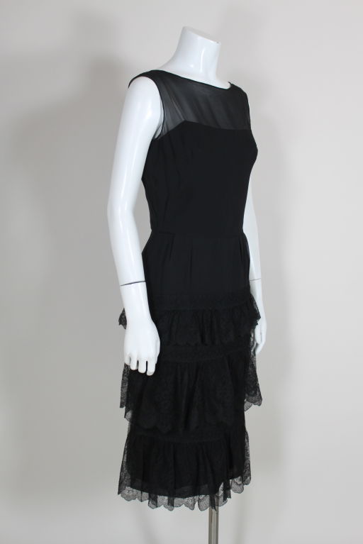 Elegant black silk chiffon cocktail dress from American couture label Mainbocher features a subtly tiered lace skirt. Sheer sleeveless crepe chiffon bodice lays over black silk lining. Dress fastens at side. Fully lined.<br />
<br
