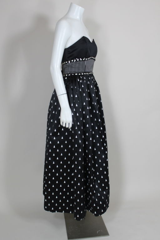 Graphic printed black satin gown from Geoffrey Beene circa 1980's. Strapless gown has a sculpted sweetheart neck. Bodice has a middle panel of printed vertically striped satin, which is trimmed in black sequins and white corded mini rosettes. Full