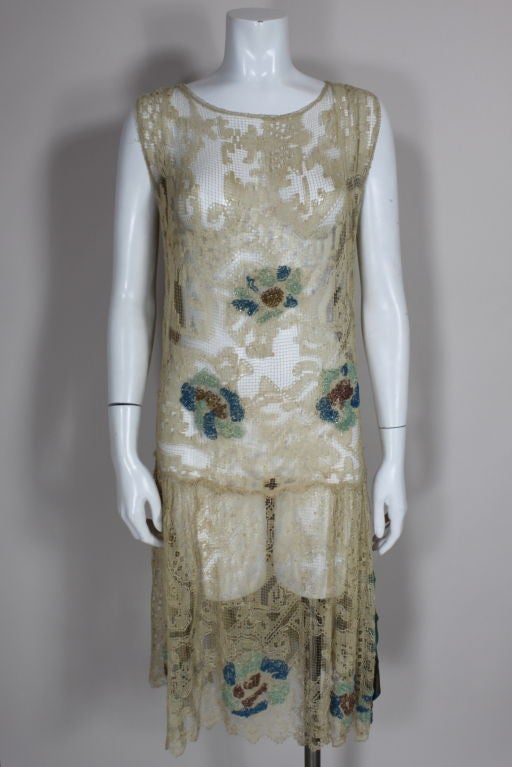 Lovely 1920's sleeveless floral cotton fillet lace dress is embellished with seafoam green, bright blue and mink brown glass beads. Skirt is accented with a decorative panel of color-blocked silk lame. Iconic drop-waisted deco silhouette.