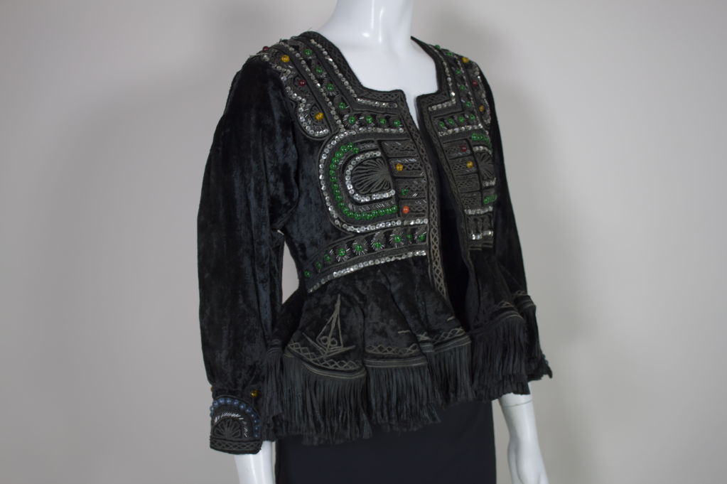 Gorgeous, heavily embellished black velvet ethnic Bolivian jacket features a ruffled peplum trimmed in black braided silk fringe. Jacket has geometric panels of embellishment which are embroidered with swirling thin steel grey bands of thread,