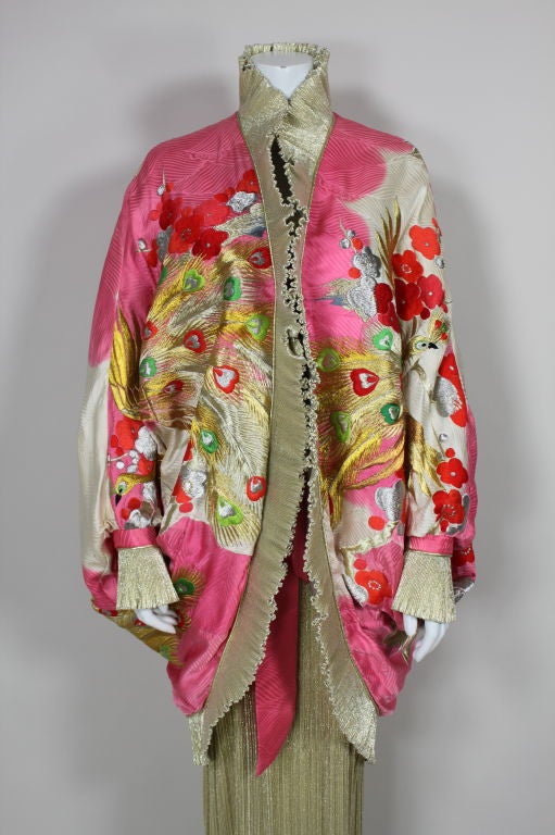 Whimsical, brilliantly colored ensemble from Amen Wardy features a dolman sleeved cocoon style jacket and a pleated column dress. Pink and white silk jacquard jacket is embroidered with metallic peacocks flying through cherry blossoms. Peacocks are