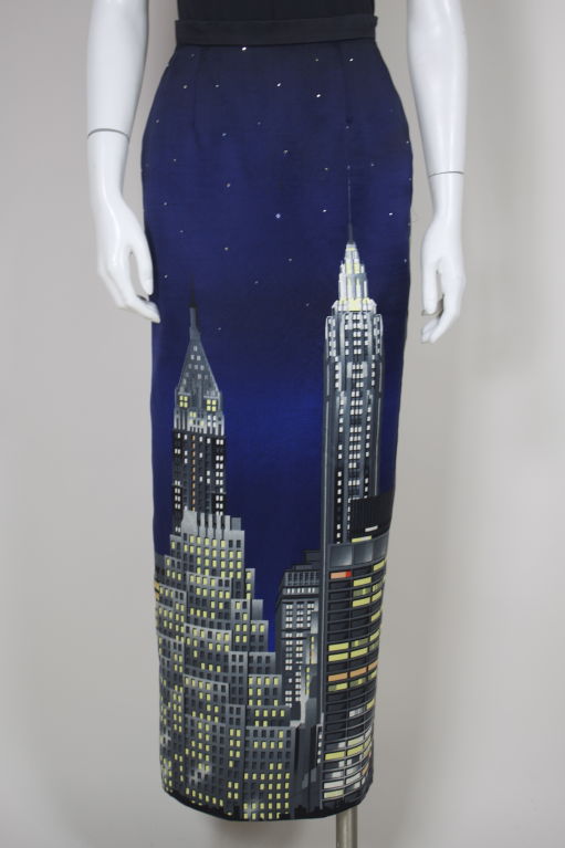 Moschino Couture silk maxi skirt features a graphic printed city skyline against an indigo background. Printed stars are embellished with studded rhinestones. Zip-back, fully lined.<br />
<br />
Measurements-<br />
Waist: 25”<br />
Hip: 36”<br