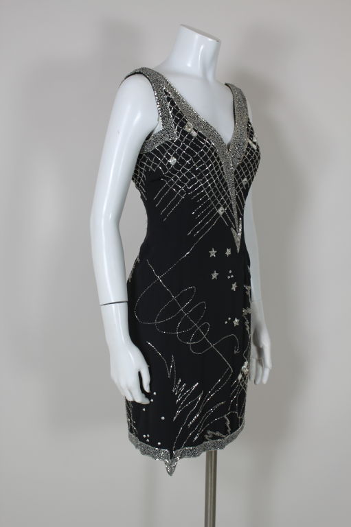 Sleeveless black silk crepe cocktail dress from Fabrice is embellished with silver lined glass seed and bugle beads in celestial geometric patterns. Faceted glass star and square sew-on gems are sprinkled all over. Bands of glass beads are sewn