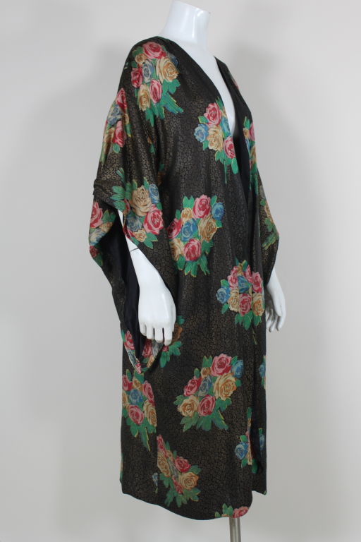 Exquisite floral gold lamé coat features a multicolored rose bouquet motif in yellow ochre, jade green, rose pink and robin’s egg blue on a black and gold ground. Collarless coat has kimono sleeves and is fully lined with lining that appears to be