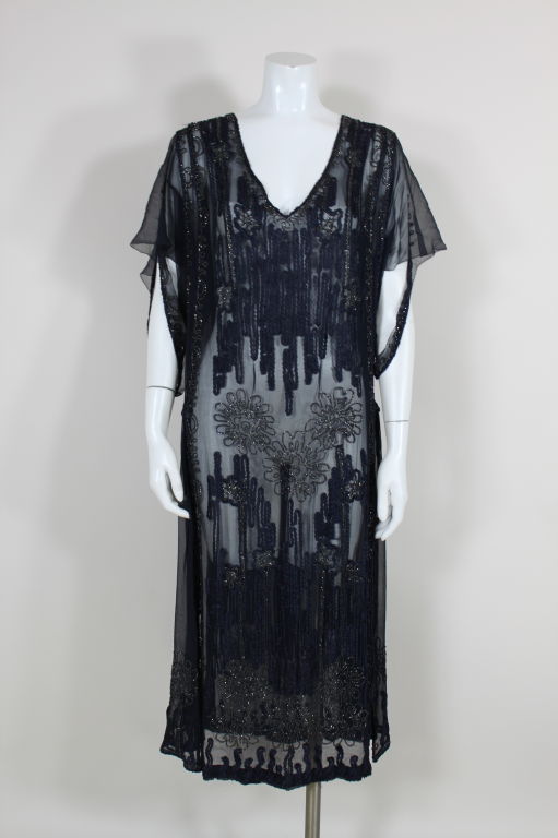 Fantastic, 1920s midnight blue chiffon dress is embellished with a twisted, braided ribbon and gunmetal glass seed beads that form organic floral shapes. Scrolling lines of beading edge all seams. Side panels are gathered at drop waist and can be