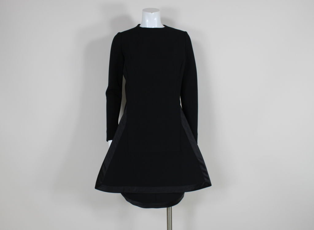 Iconic 1960s black wool long sleeved dress from Pierre Cardin features a Space Age inspired geometric panel that extends beyond the body of the dress. Triangular panel attaches at princess seams and is trimmed in a band of black satin. Decorative