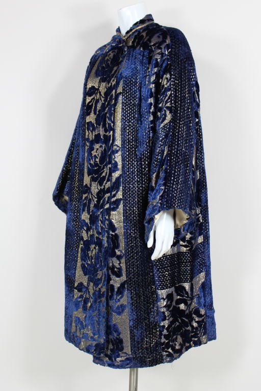 Amazingly beautiful dark sapphire blue devoré silk velvet and gold lamé opera coat features an art deco floral pattern framed by wide bands of geometric panels. Coat has wide kimono style sleeves and asymmetrical collar that fastens with a fabric