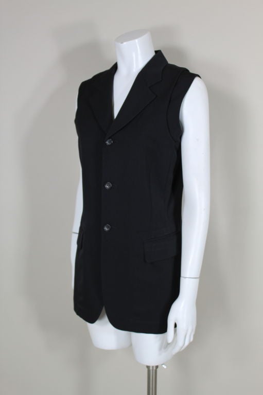 Iconic wool twill single-breasted vest from Comme des Garcons puts an avant-garde spin on the conventional waistcoat. Vest features a doubled shoulder panel in which the top layer of the garment is seamed to another layer to create two armscyes.