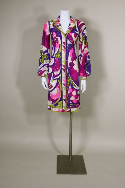 Iconic, printed silk empire waist dress from Pucci features a geometric psychedelic floral print in violet, fuschia, hot pink and lime green. Sleeves balloon over fitted cuffs. Dress buttons closed with a hidden front placket. An Op-Art