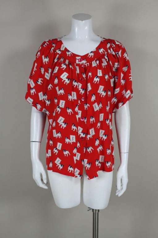 Vibrant red silk blouse from Yves Saint Laurent features an adorable french bull dog print. Modified batwing sleeves are elasticized at hem. Button front placket. <br />
<br />
Measurements-<br />
Bust: up to 48