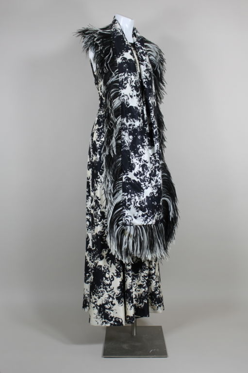 Circa 1960's silk twill gown has a clean, modern silhouette that is fitted through the bodice and flares into an a-line skirt. A bold black and white all-over feather print is echoed by the ostrich feathers that trim the wrap. Bodice has