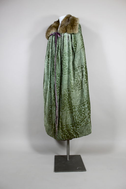 Unbelievable sage green cut velvet 1920's opera cape features alternating panes of geometric and fleur de lis motifs. Cape is lined with lavender velvet, collar is lined with luscious fur. <br />
<br />
Measurements-<br />
Length from Center Back