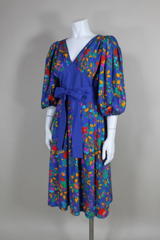 Summery late 1970's/early 1980's Yves Saint Laurent Rive Gauche cotton peasant dress is printed with a brightly colored floral motif in an Eastern European inspired color palette featuring shades of yellow, fuschia, red and green on a cerulean blue