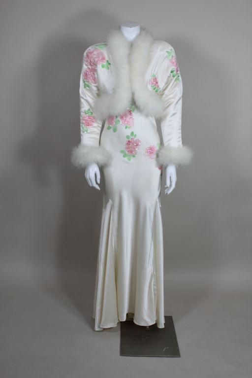 Sexy and glamorous, this ethereal 1970's white silk satin bias cut gown from Bill Tice is printed with painterly pastel roses accented with iridescent sequins. Matching silk jacket is trimmed in lush marabou feathers and features quilted roses