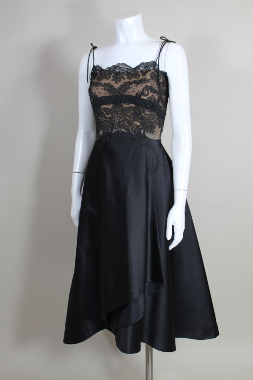 Fabulous cocktail dress from legendary costume designer, Irene, features a bodice of black chantilly lace laid over nude silk, and a skirt of black silk satin that is draped with a structural swag.  Edges of lace are appliquéd onto skirt for added