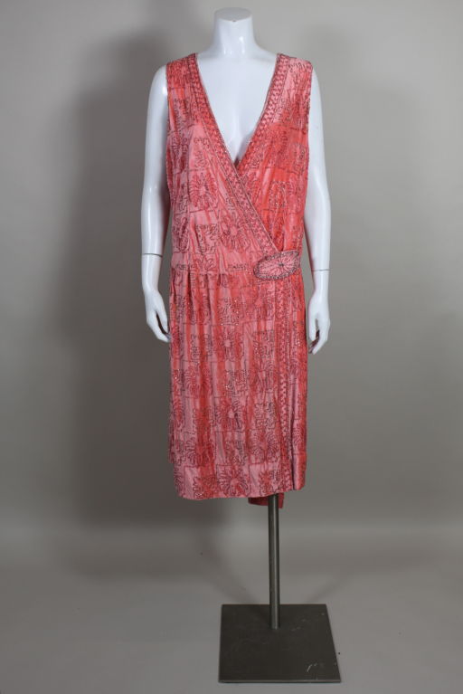 This fantastic, vibrant, peachy luscious coral silk-velvet 1920s piece is the ultimate flapper party dress. It is embroidered all over with rosy pink and gunmetal gray glass beads in a deco floral pattern. The wrap bodice snaps in the front and is