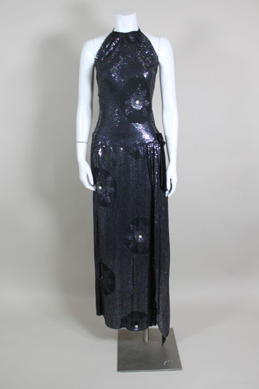 Gorgeous, slinky 1980's black crepe gown is entirely embroidered with iridescent micro sequins in dark peacock blue. Rounded sections of chiffon surround floral motifs sewn from textured paillettes and micro pearls. Fitted gown is slit up to the