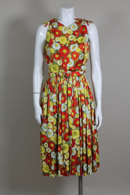 This beautiful 1960's cocktail dress from Traina-Norell is printed with a vibrant, summery daisy pattern in shades of poppy red, sunny yellow and white. Shoulders are accented with decorative bows, skirt is pleated from the waist for fullness. Comes