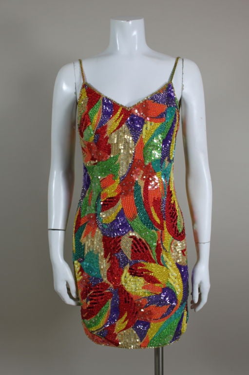 Fantastic 1980’s cocktail dress from Oleg Cassini features a multi-colored kaleidoscopic print on silk chiffon embellished with glass beads & sequins in brilliant, tropical shades of red, teal, gold, orange, purple and turquoise. Beads and sequins