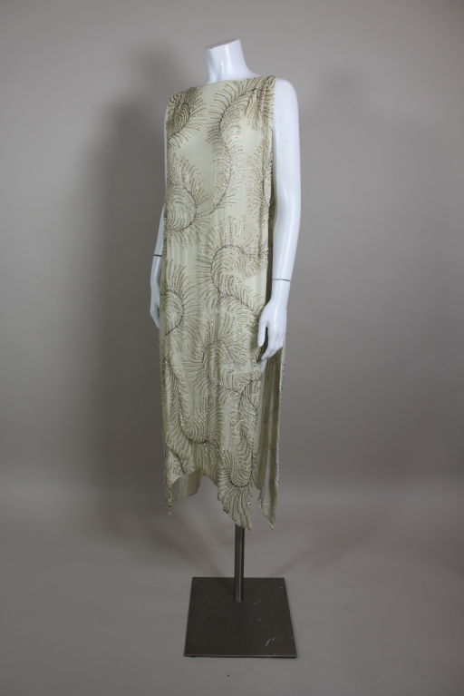 Amazingly beautiful ivory silk chiffon tabard-style 1920's dress is embroidered with a swirling feather motif done in micro pearls, crystal rhinestones, and metallic glass beads. Dress is open on the sides with an elegant boat neck. Hem is curved