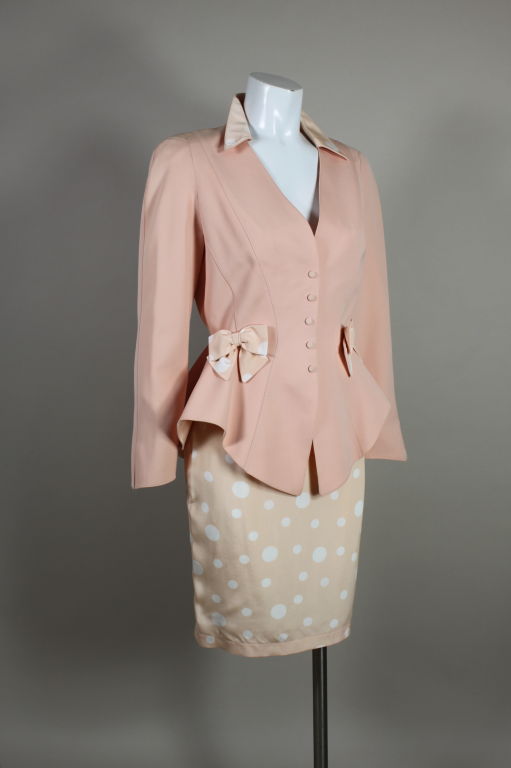 Fabulous, iconic skirt suit from Thierry Mugler features a blush pink jacket and polka dot silk skirt. Mugler's signature seaming shapes the jacket into a wasp-waist silhouette with flared peplum. Contrasting polka dot silk bows accent the waist.