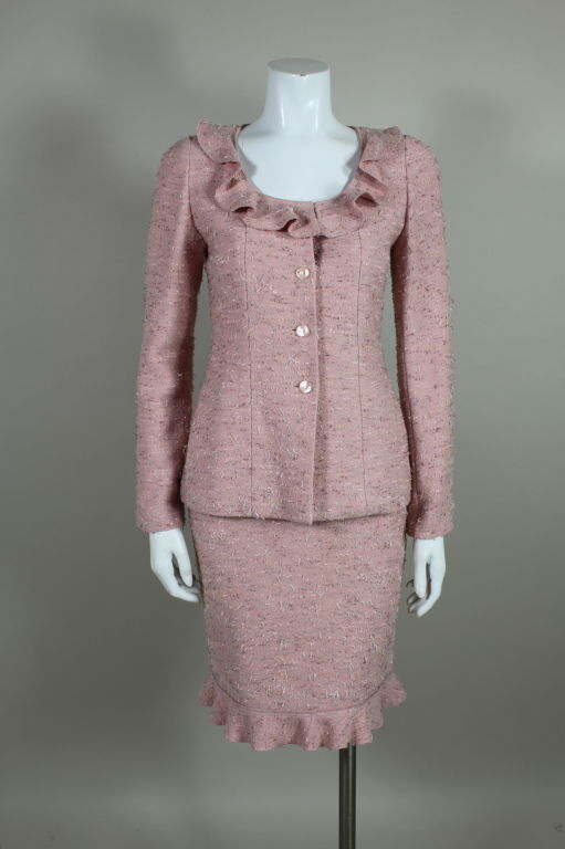 Fabulous two piece suit from Chanel is done in a light weight rose pink wool tweed speckled with woven earth-tone fibers. Jacket is trimmed with a ruffled collar and skirt is hemmed with a ruffled edge. Monogram lucite logo buttons have suspended