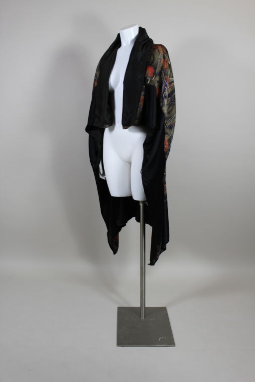 Absolutely stunning art deco cape is made from a beautiful silk lamé brocade with an abstracted water lily motif. Streaks of color swirl across a geometric gold patterned ground. Panels of black silk satin trim the edges. The fabric is gathered up