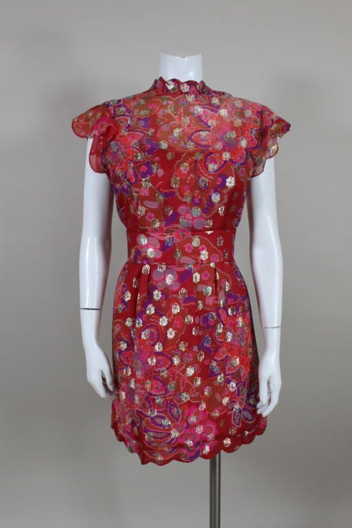 Party perfect 1960's cocktail dress from American designer Tina Leser is done in a floral organza woven with gold metallic lamé spots. Flutter sleeves and mandarin collar have scalloped edges. Comes with matching belt that fastens at the waist with