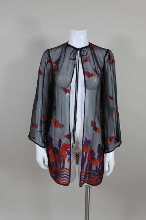 Diaphanous and sexy 1970s chiffon jacket is woven with an iris and butterfly motif in fiery sunset shades of red, orange and violet. Chiffon is trimmed in braided silk cording. Ties at the neck, open front.