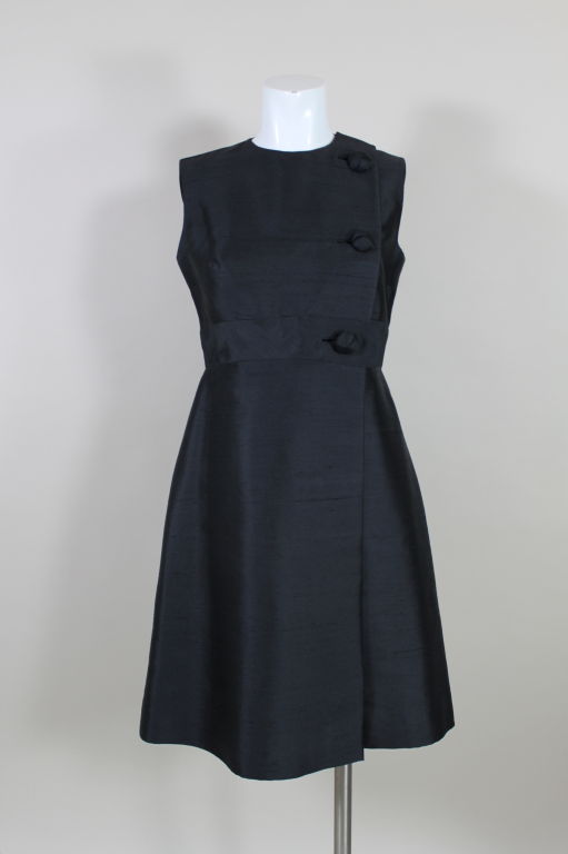 Sleek and elegant black raw silk cocktail dress from Anne Fogarty is fashioned in an early 1960’s silhouette with a double breasted front closure. A single row of large statement  buttons in a knot style fasten the front of the dress. Skirt has a