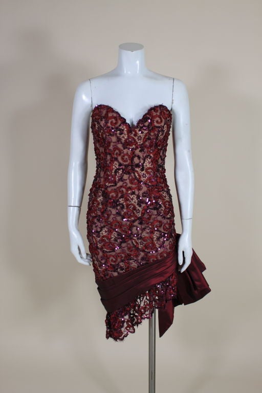 This fabulous 1980's cocktail dress, attributed to iconic American designer Bob Mackie, is covered in bordeaux red metallic lace embellished with silk ribbon and iridescent sequins. Sculpted, strapless bodice has a sexy plunging neck and