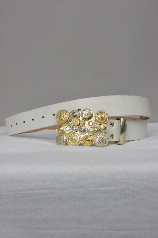 White leather belt with a large, Western style goldtone buckle decorated with assorted metal buttons.

Buckle is 4