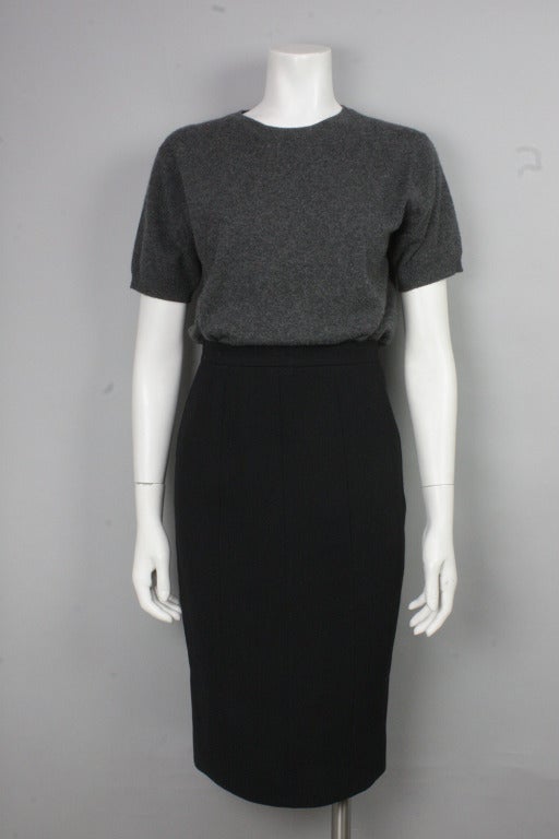 Classic and flattering black wool pencil skirt with buttoned back slit. Buttons are black with a gold-tone center and delicately etched with the interlocking C's logo. Zip and clasp at back for closure. Lined in silk.
