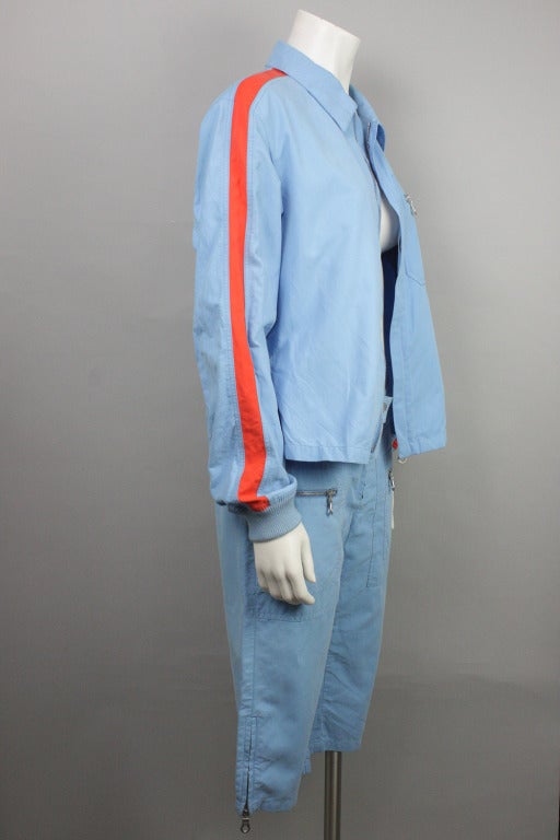 Now on sale! Original price $1100

Blue two piece set of low-waisted cropped pants and zip up jacket with orange accents and interlocking C's logo on jacket's breast and on one pant leg. Circa 2002 from Chanel's Identification line.