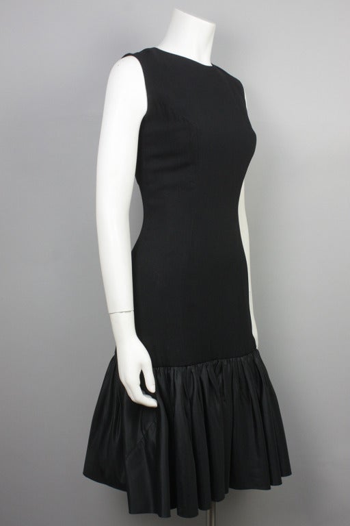 Fitted black '50s dress with flounce and bow in contrasting fabric at hem. Wool crepe body with poly satin