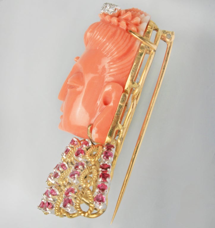 A beautifully crafted and serene image of Quan Yin, Goddess of Compassion, elegantly made of salmon colored coral, 18K gold, 40 rubies, with a tiara of seven diamonds.