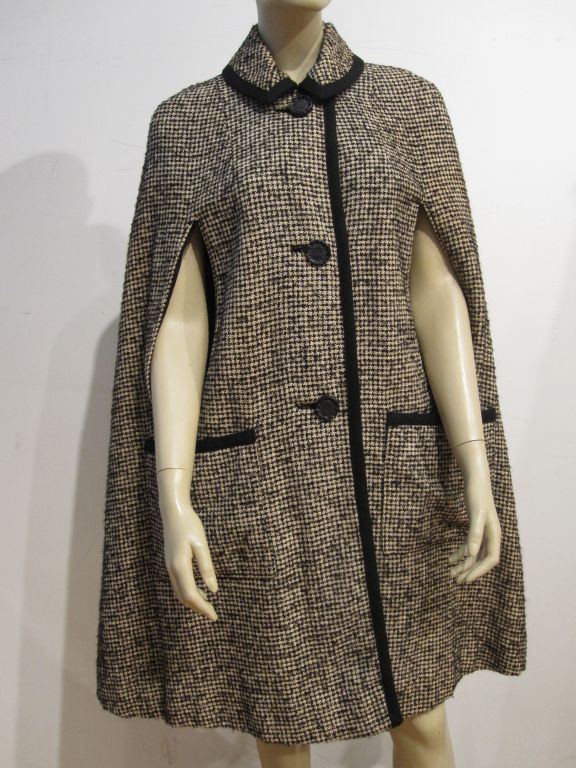 A natty little 60s tweed cape edged in black braided trim. Two front pockets and arm slits.