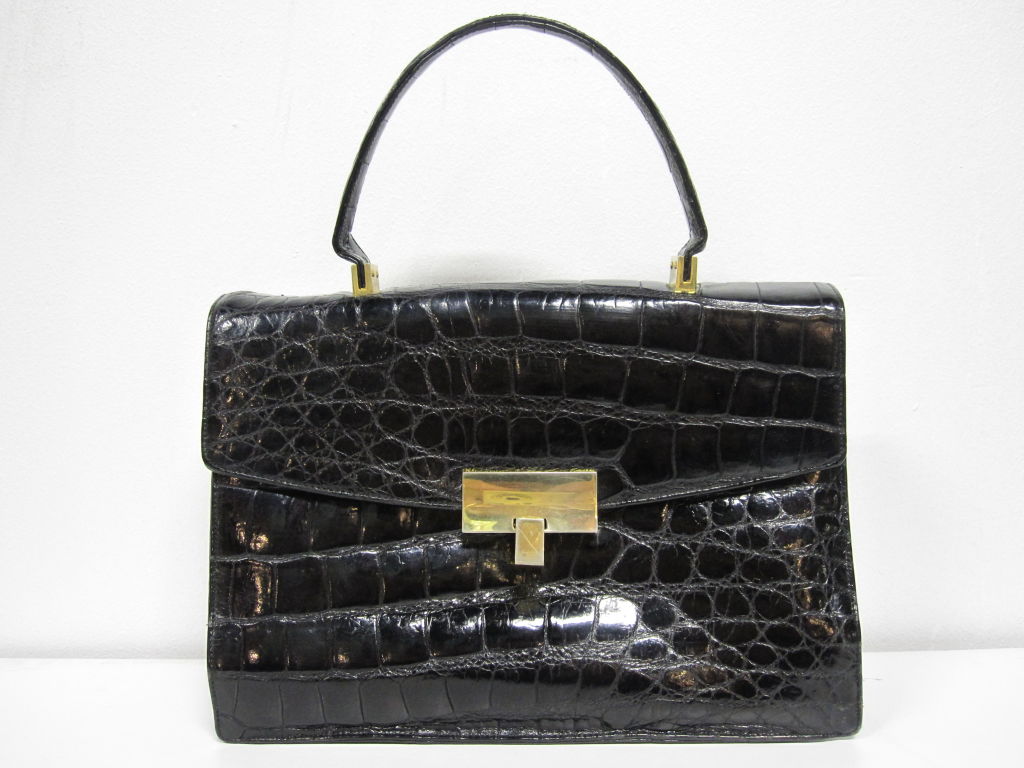 A wonderful, tailored, structured 60s Koret black alligator handbag with gold-tone hardware, red leather lining, attached leather coin purse and a handle in excellent condition.  Measures 10.5