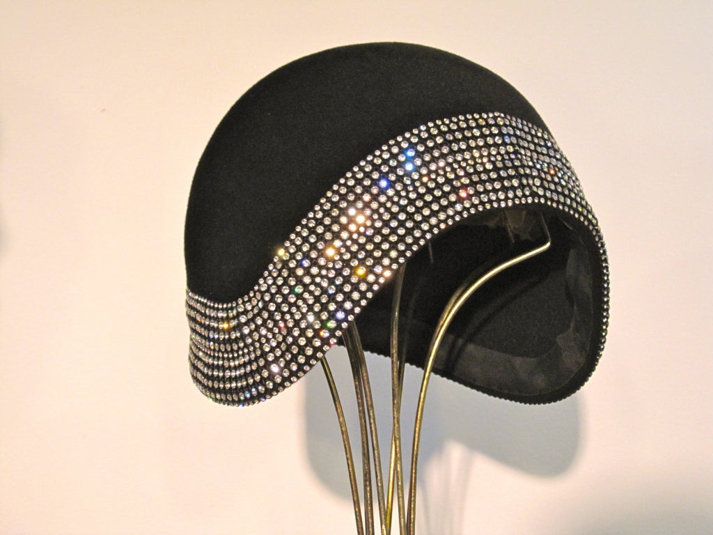 A fantastic, mint condition Leslie James cloche from the 60s, styled a la the 1920s of black felt with a wide, bright band of rhinestones all the way around.  A medium size.  (22)<br />
<br />
Gorgeous!