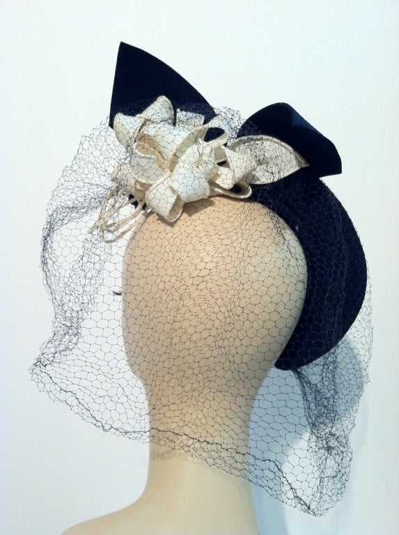 A wonderfully sweet 1940s hat in navy blue felt:  Half-hat style with a large bouquet under brim on right side and intact veil. Very pretty and unusual. One Size.